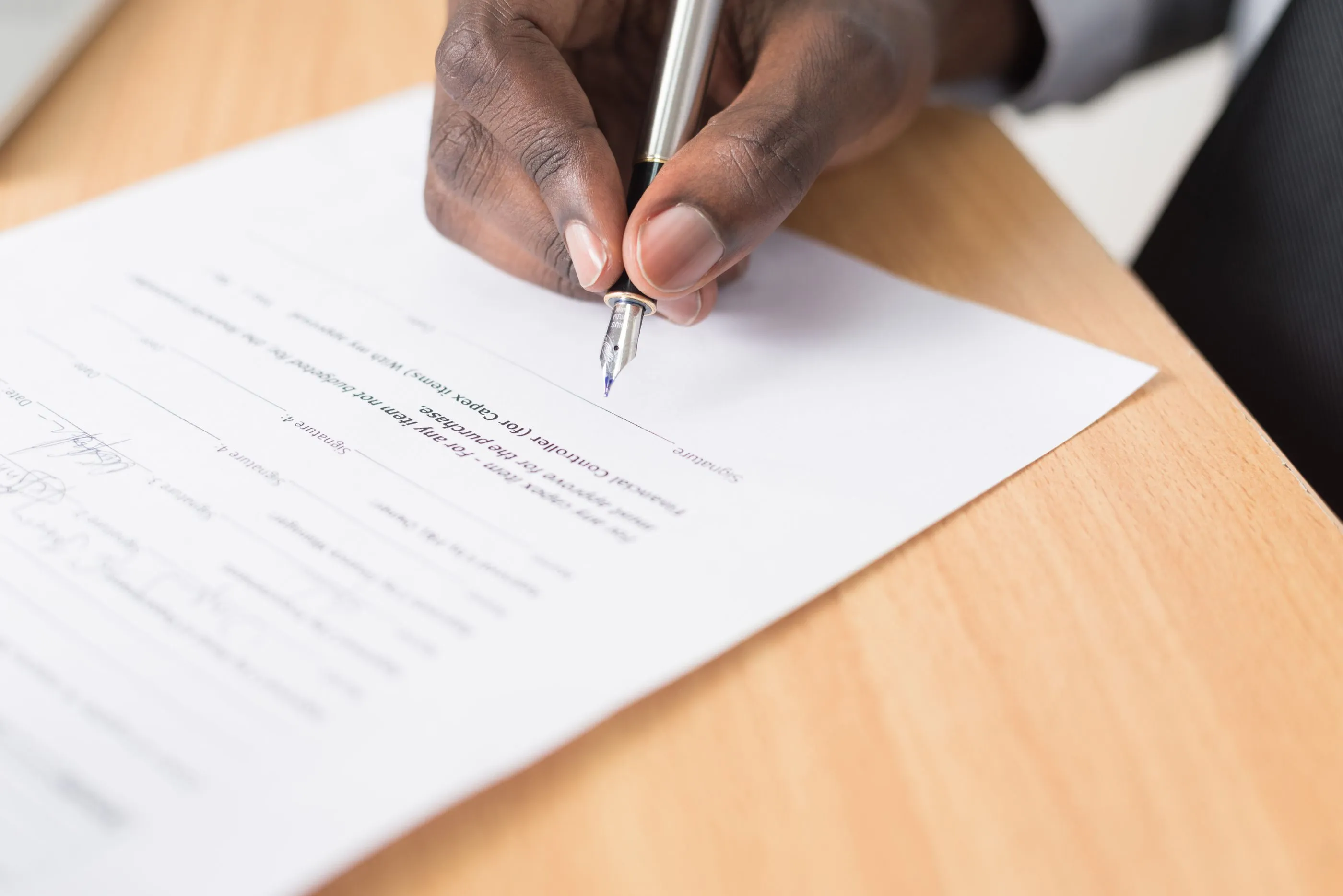 A hand signing paperwork with a fountain pen at a desk, the moment a landlord entrusts the letting to us.